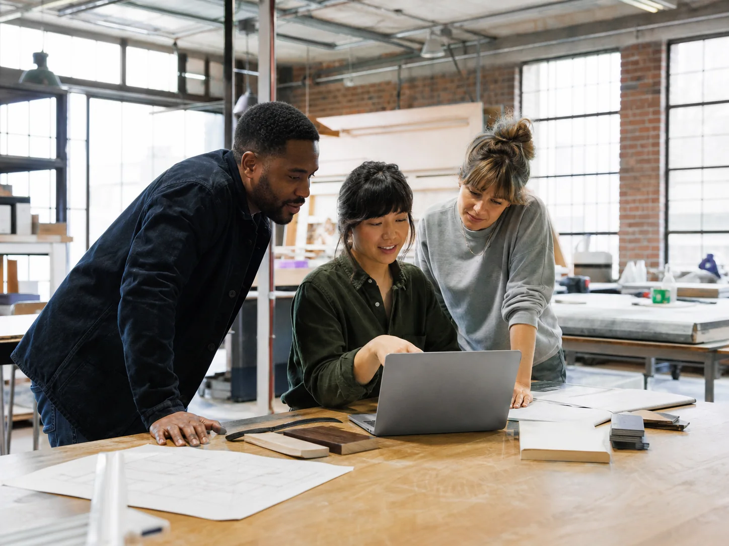 Detroit design and fabrication team collaborating around a laptop in a brick workshop