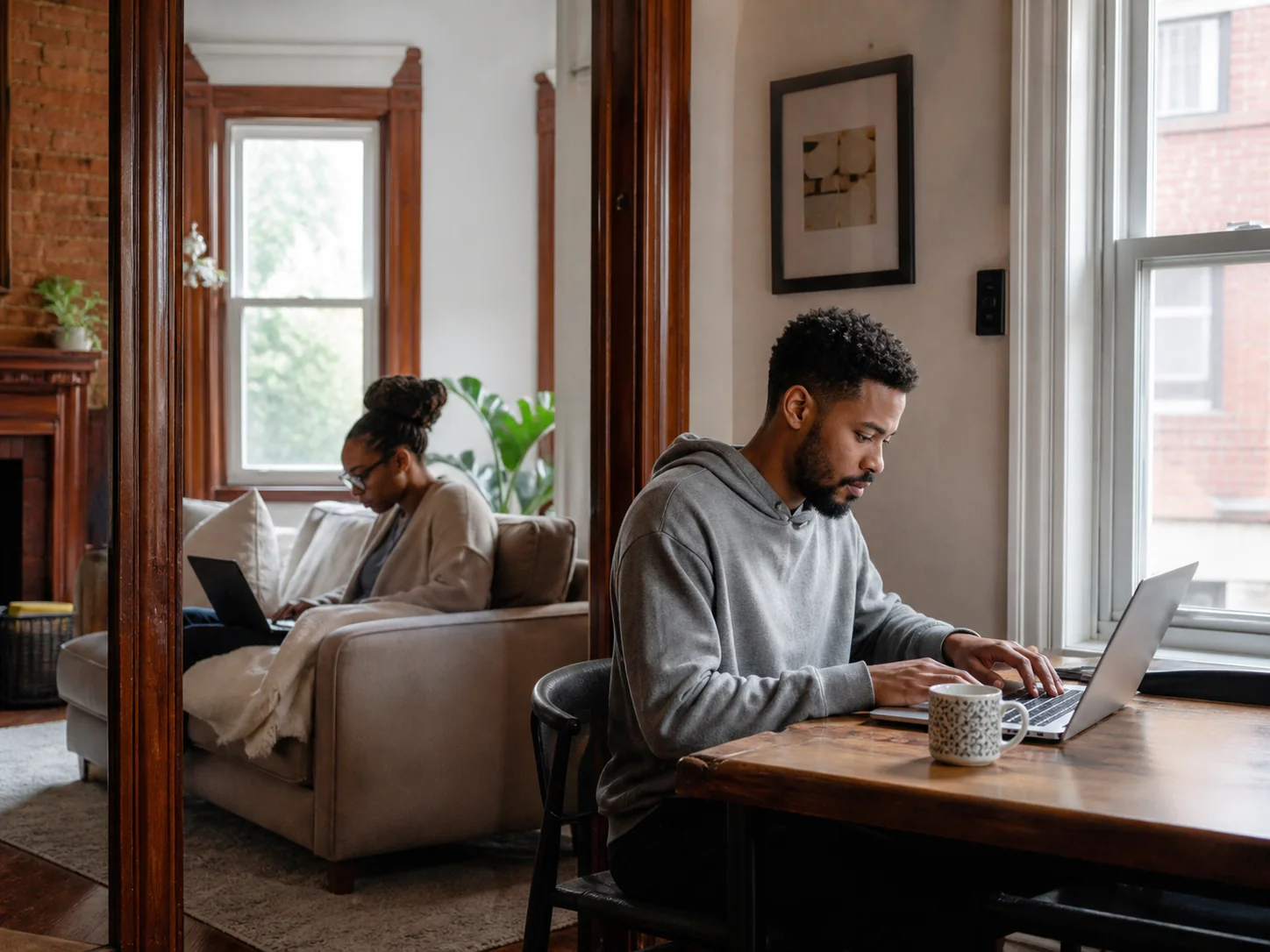 Two Detroit residents working online from separate rooms in a renovated brick home